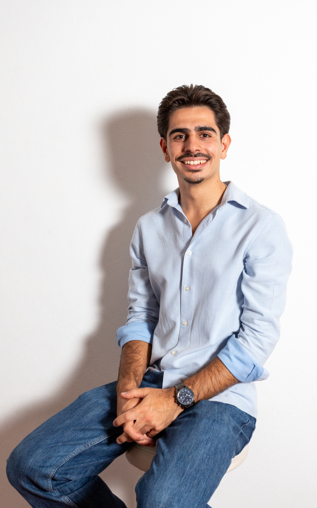Retrato profissional de Afonso Tavares Marques sentado, com camisa azul clara e fundo branco
